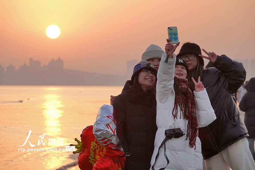 2025年1月1日，在山東省煙臺市萊山區海濱，游客們與新年第一縷陽光合影。唐克攝（人民圖片網）