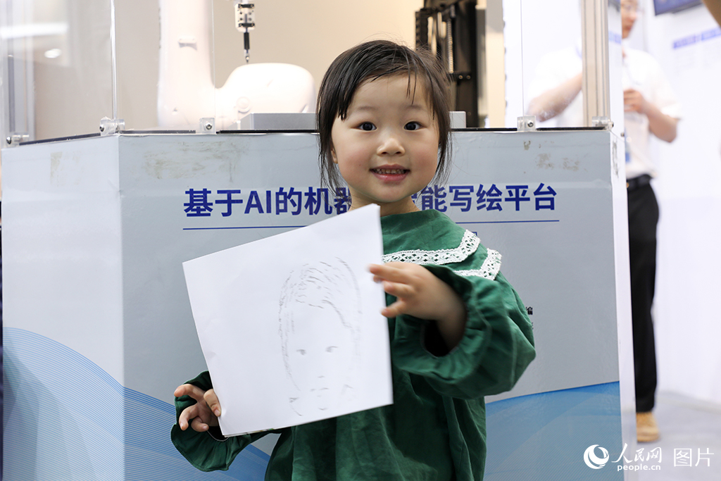 2024年4月15日，福建省福州市，在第61屆中國高等教育博覽會上，一名小朋友拿著機械臂為她畫的頭像，露出開心的笑容。人民網 黃東儀攝