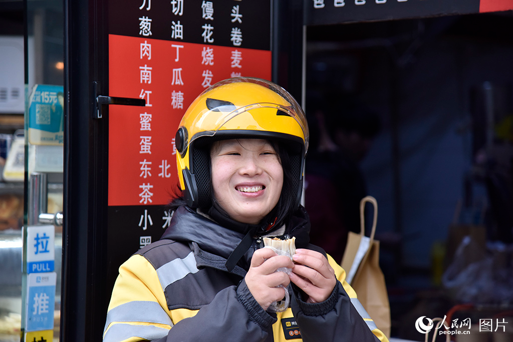 2024年12月25日上午，在上海市，外賣員黃夢丹結束了忙碌的“早高峰”配送。在她每天必經的早餐鋪，買了一個熱氣騰騰的燒麥，溫暖的美食讓她臉上洋溢著幸福的笑容。人民網記者 龔莎攝