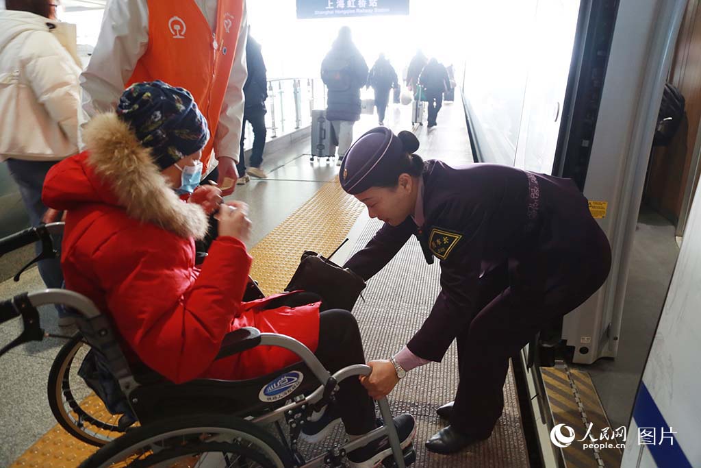 2025年春運首日，上海虹橋站站臺上，一位坐輪椅的乘客在乘務員的幫助下登車。人民網記者 龔莎攝