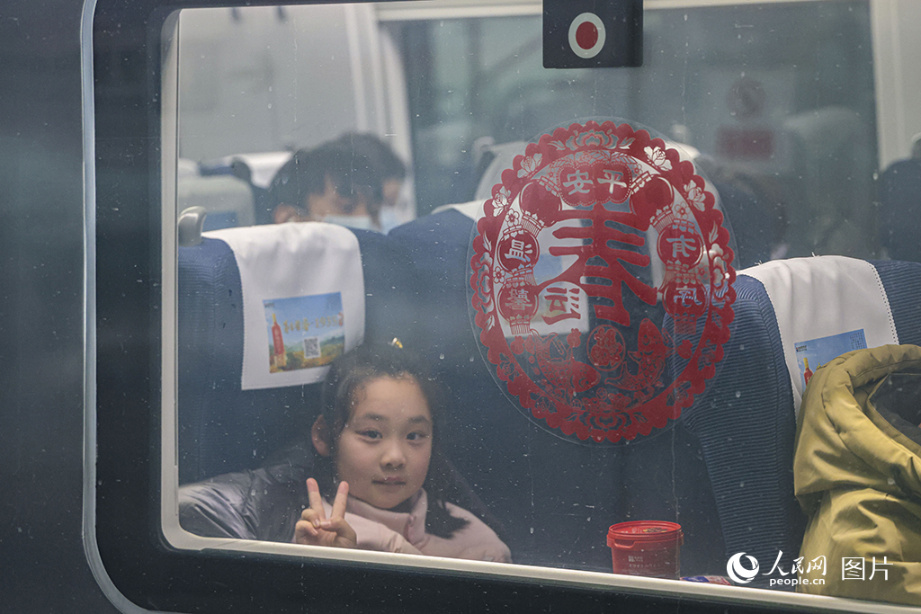 2025年春運首日，上海虹橋火車站，一位小旅客坐在即將開行的列車上，隔著玻璃窗對鏡頭比耶。人民網記者 王初攝