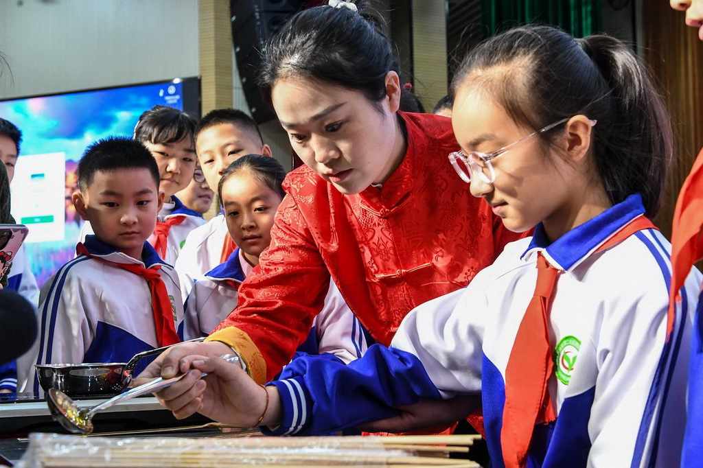 2月24日，在吉林省第二實驗朝陽學校，糖畫藝人董露露（右二）指導學生制作糖畫。