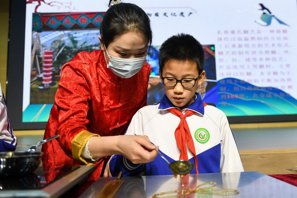 2月24日，在吉林省第二實驗朝陽學校，糖畫藝人董露露（左）指導學生制作糖畫。