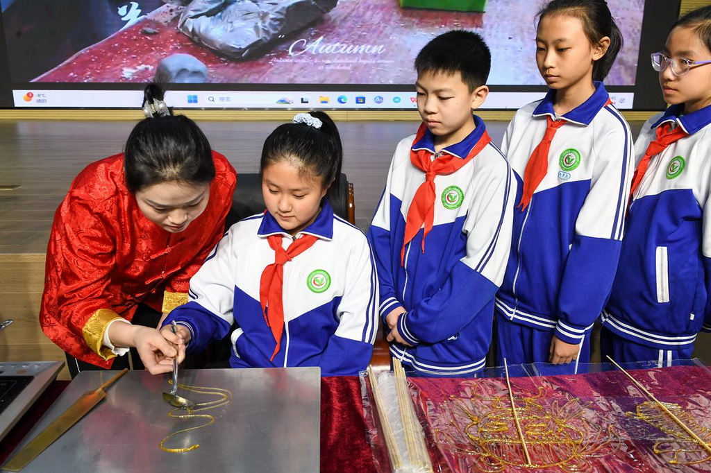 2月24日，在吉林省第二實驗朝陽學校，糖畫藝人董露露（左一）指導學生制作糖畫。