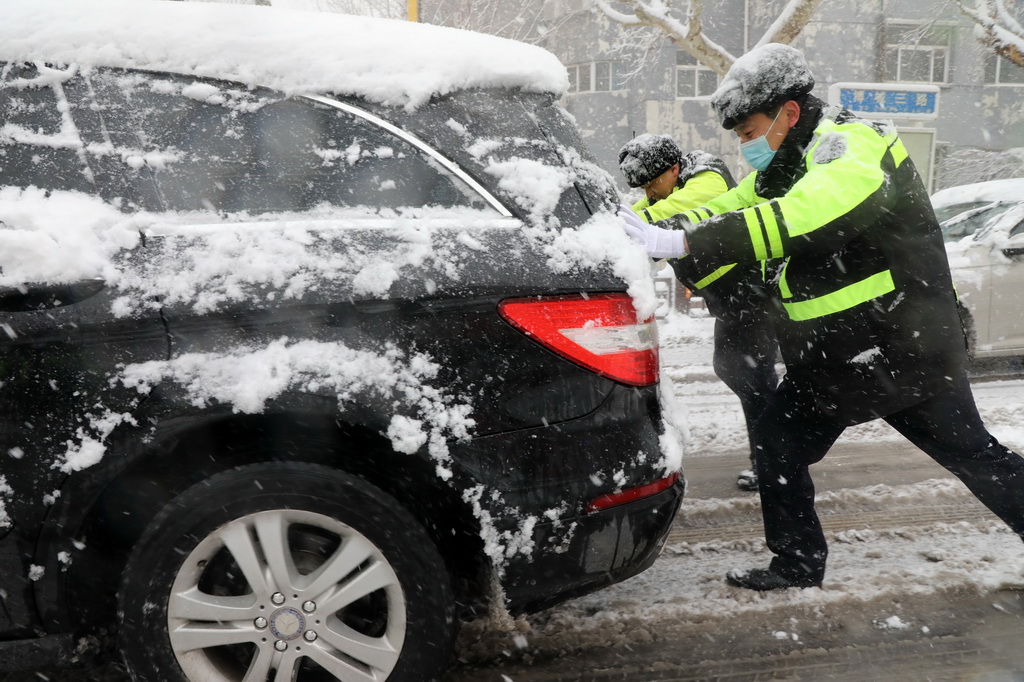 3月2日，在山東省濱州市博興縣城區街頭，執勤交警在雪中幫助市民推車。新華社發（陳彬攝）