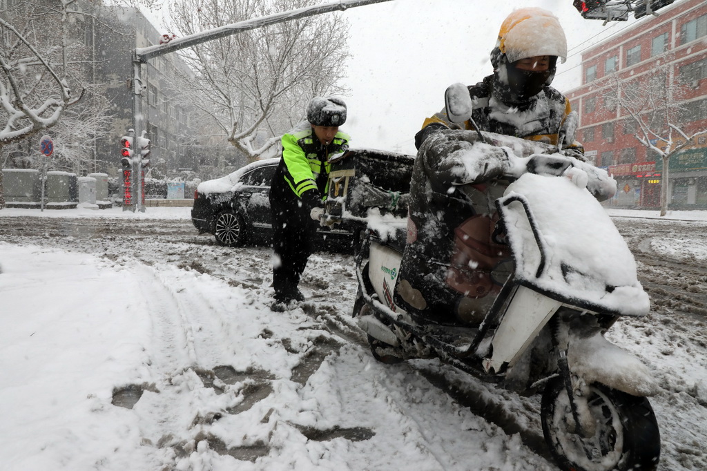 3月2日，在山東省濱州市博興縣城區街頭，執勤交警在雪中幫助一外賣小哥推電瓶車。新華社發（陳彬攝）