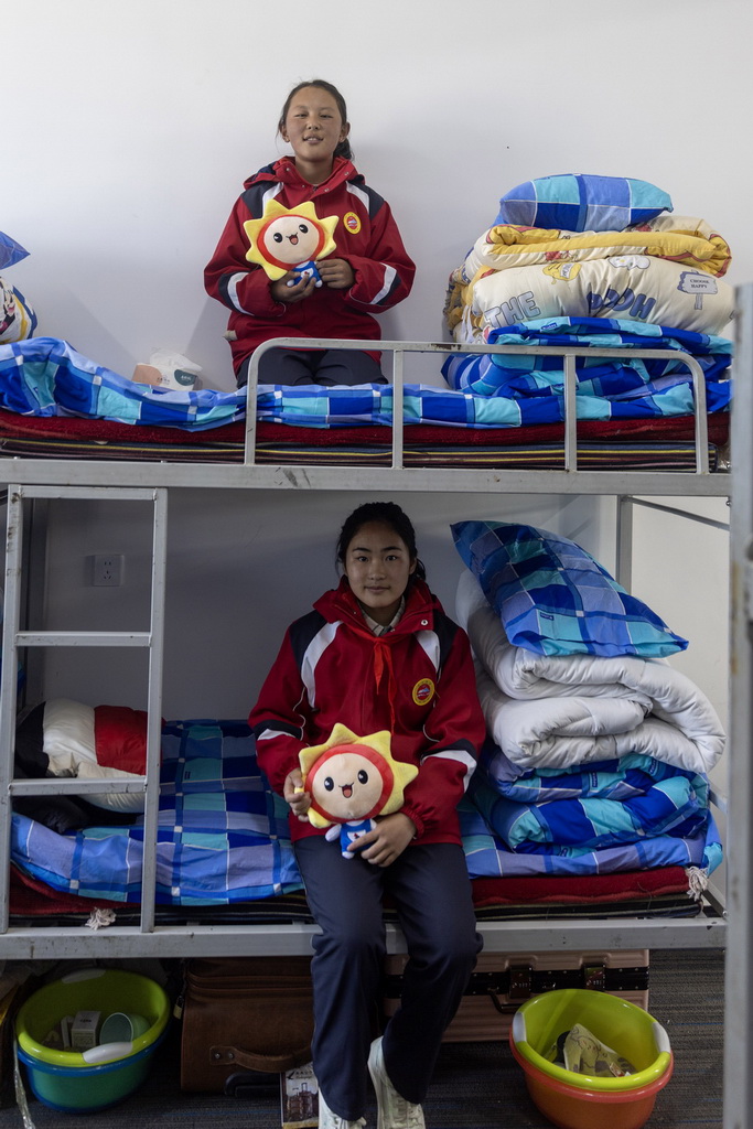 來自定日縣措果鄉小學的學生旦增曲珍（上）和白瑪（下）在定日縣委黨校分流安置點的宿舍里展示老師們為她們準備的“太陽娃娃”毛絨玩具（3月4日攝）。