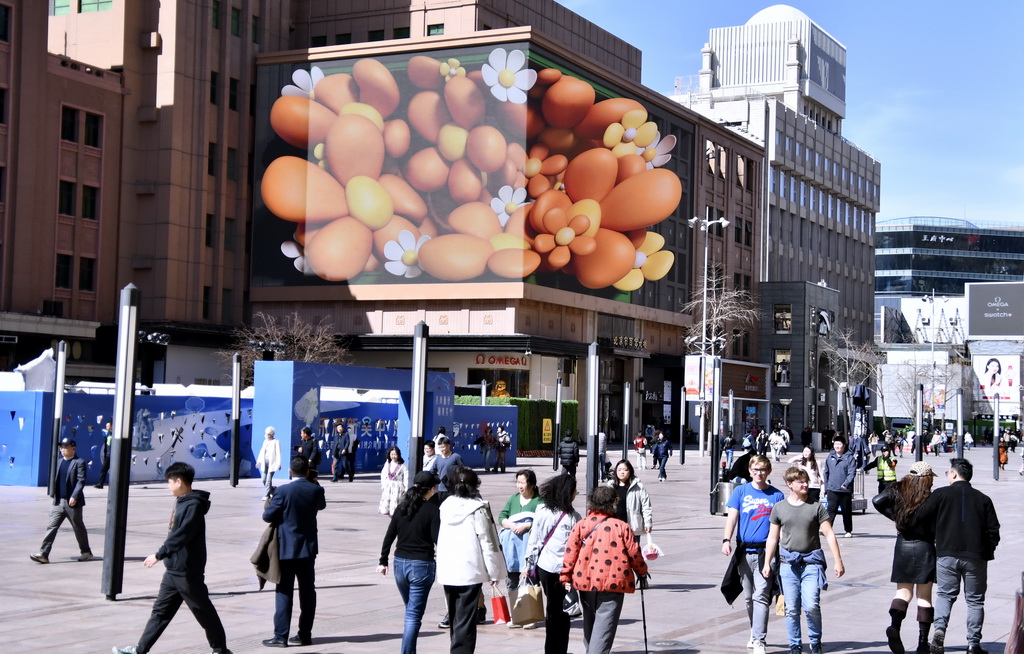 3月20日，人們從北京王府井商業街區的裸眼3D大屏前走過。