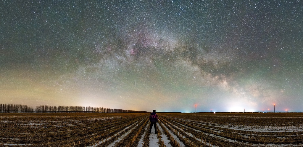 3月29日凌晨，一名游客在黑龍江省富錦市觀賞“銀河拱橋”（拼接照片）。新華社發（曲玉寶攝）