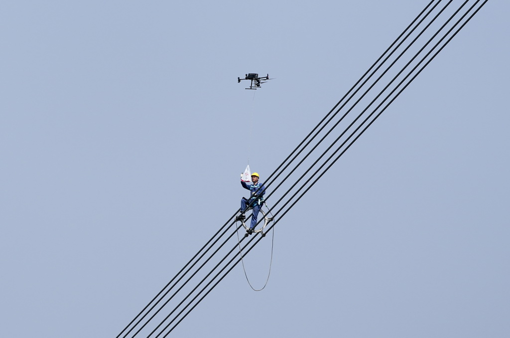4月8日，在重慶市合川區“疆電入渝”特高壓工程重慶段走線驗收現場，國網重慶超高壓公司地面工作人員利用無人機將礦泉水送給線路驗收人員。新華社記者 劉潺 攝