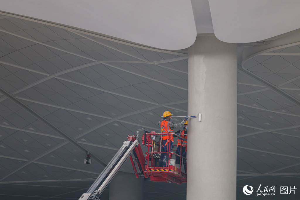 工人在施工現場粉刷樞紐主體結構內的柱子。