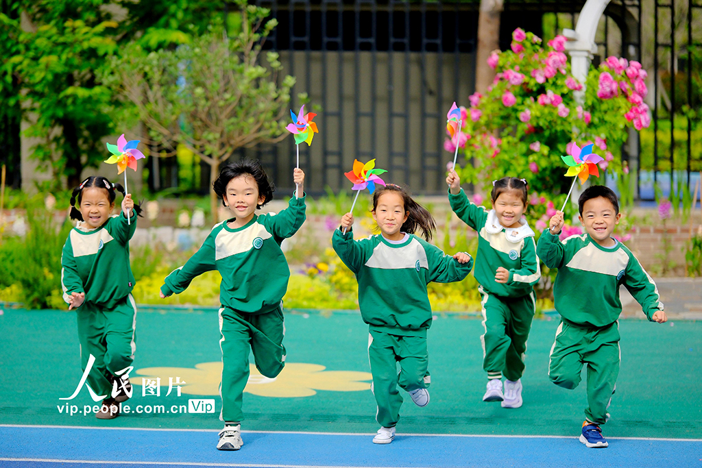 2025年5月8日，在江蘇省南通市，崇川區沁園幼兒園的小朋友手持小風車在操場上微笑著奔跑。徐培欽攝（人民圖片網）