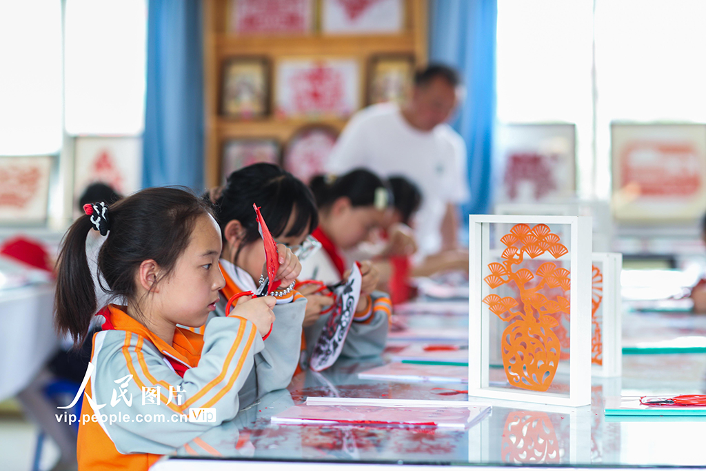 2025年5月17日，在陜西省旬邑縣逸夫小學，學生在老師的指導下學習剪紙。