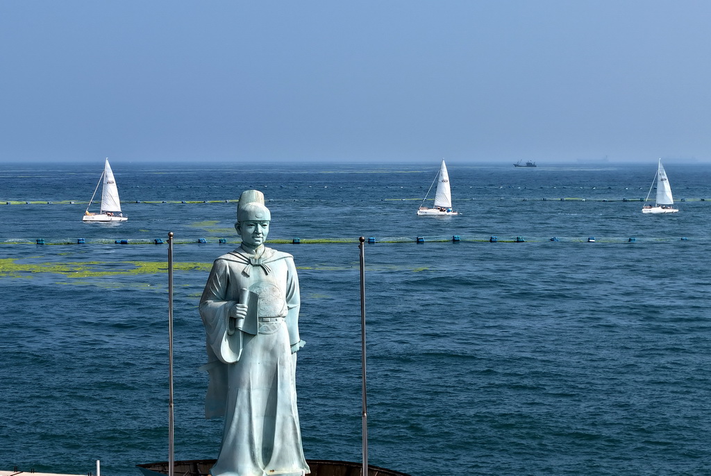 青島銀海大世界港池外，參加海上巡游的帆船從鄭和雕像旁駛過（7月10日攝，無人機照片）。