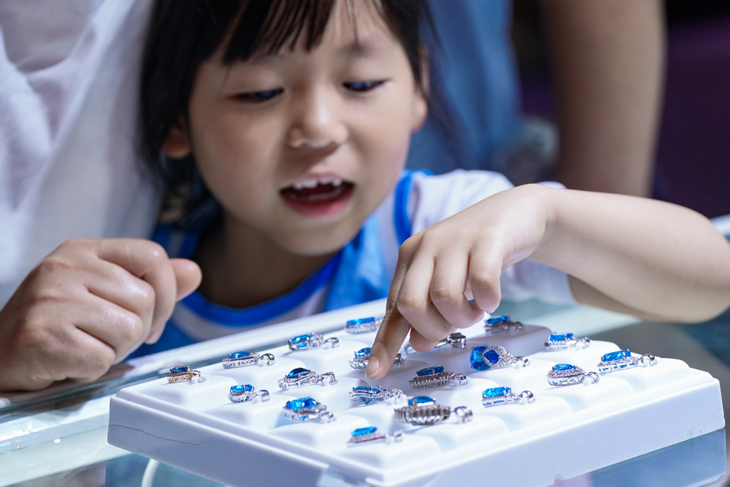 7月10日，小朋友在昆明石博會上幫家長挑選玉石。
