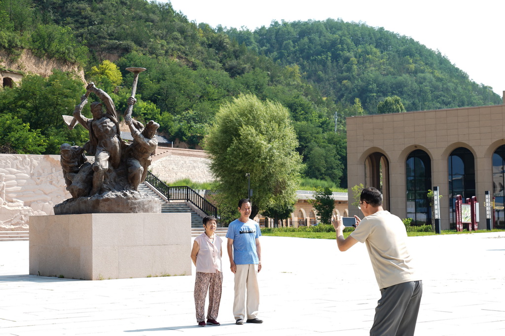 游客在南泥灣大生產紀念廣場的雕塑前合影（7月29日攝）。