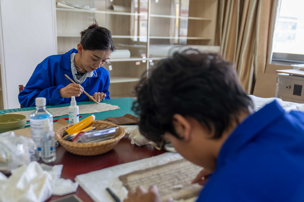 西藏自治區古籍保護中心古籍修復員次仁央宗（左）與同事對古籍進行除霉（2025年8月13日攝）。新華社記者 晉美多吉 攝