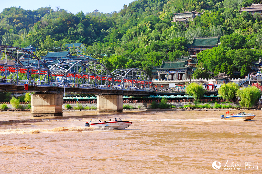9月9日，黃河邊，茶攤上飄著“三炮臺”的玫瑰香氣，百年鐵橋紅燈籠高懸，水鳥翩躚，游人沿河道悠然漫步。在蘭州，黃河南北兩岸山脈綿延，分別為北部山區和南部山區，俗稱“南北兩山”。近年來，甘肅省蘭州市積極推動黃河流域生態保護與高質量發展，持續加強生態修復，綠色發展成效不斷鞏固。截至目前，南北兩山綠化面積已達62萬余畝，1.6億多株苗木在黃河水的滋養下茁壯成長，形成了較為完善的人工林生態體系。該體系每年可減少泥沙淤積超過56萬立方米，全市水土保持率提升至71%以上，生態效益顯著。人民網記者 焦隆攝