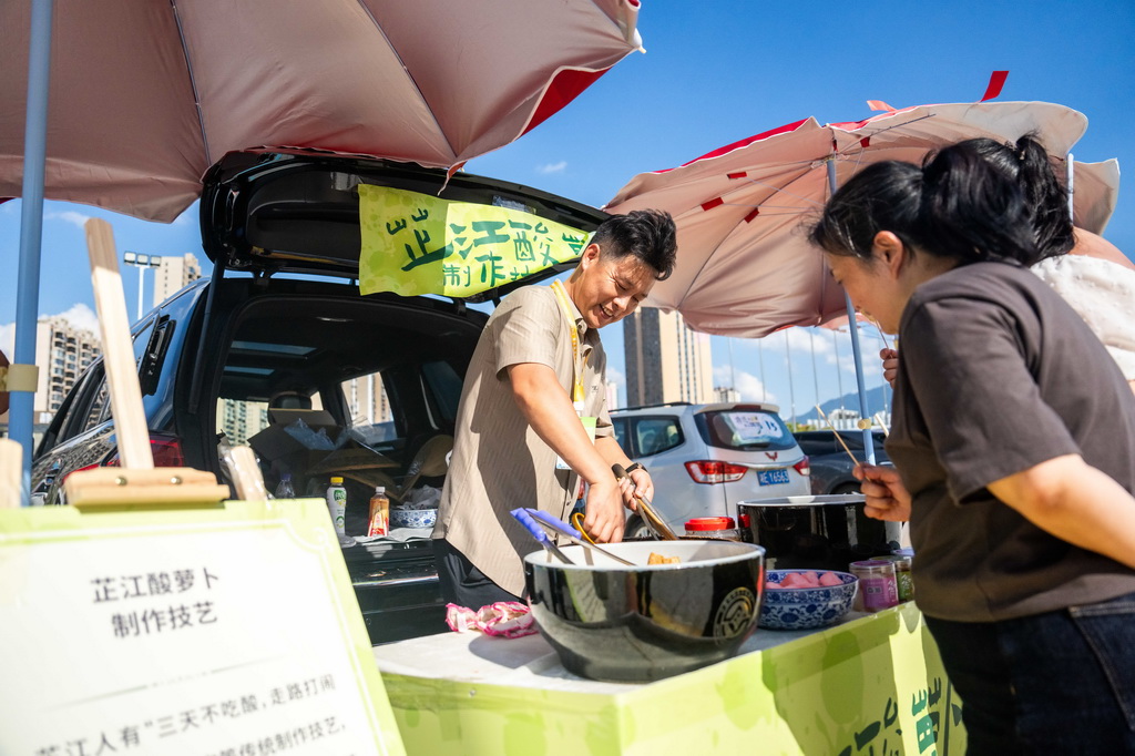 9月16日，在湖南省懷化市五溪非遺園，游客（右）在后備箱非遺市集品嘗芷江酸蘿卜。
