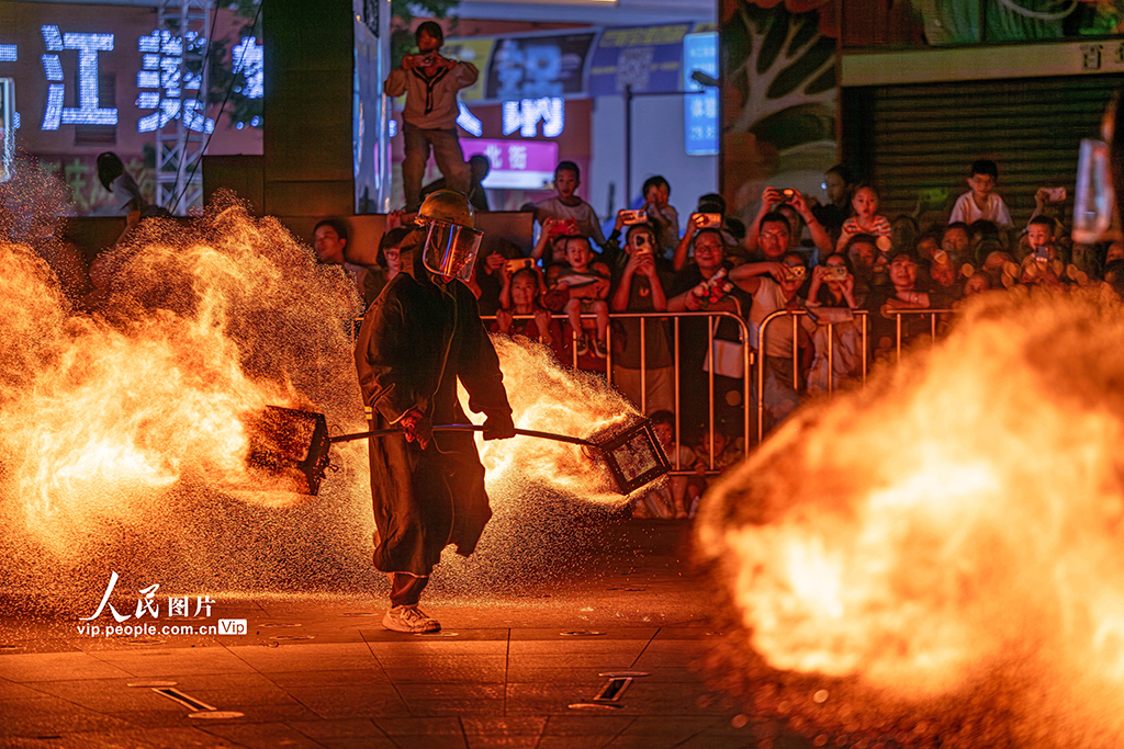 10月1日，在四川省眉山市仁壽縣懷仁街道棲西里商業街廣場，民間藝人正在表演“火壺”技藝，引得不少市民和游客駐足觀看。潘帥攝（人民圖片網）