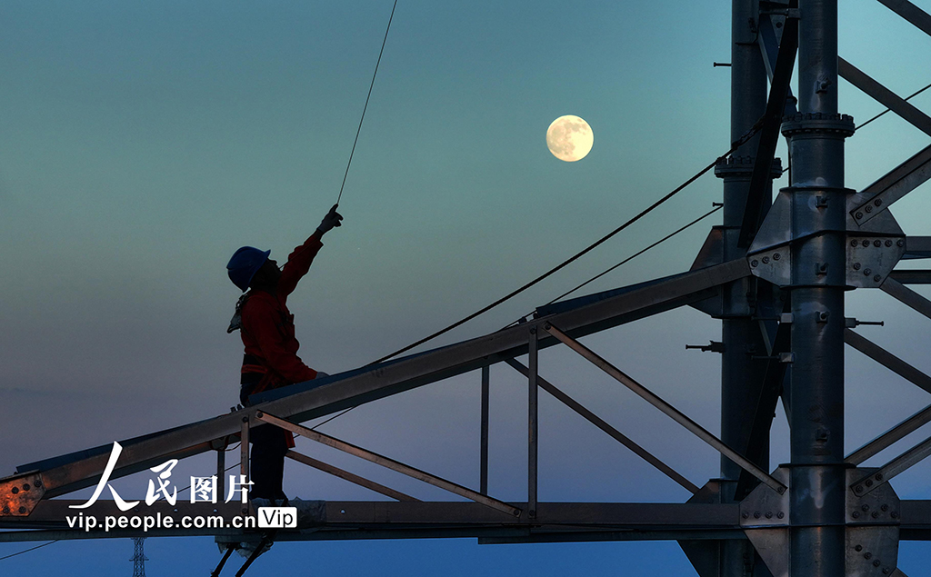 10月6日，在湖南省衡陽市雁峰區南三環路上，施工人員在高塔進行架線施工作業時與圓月同框。曹正平攝（人民圖片網）