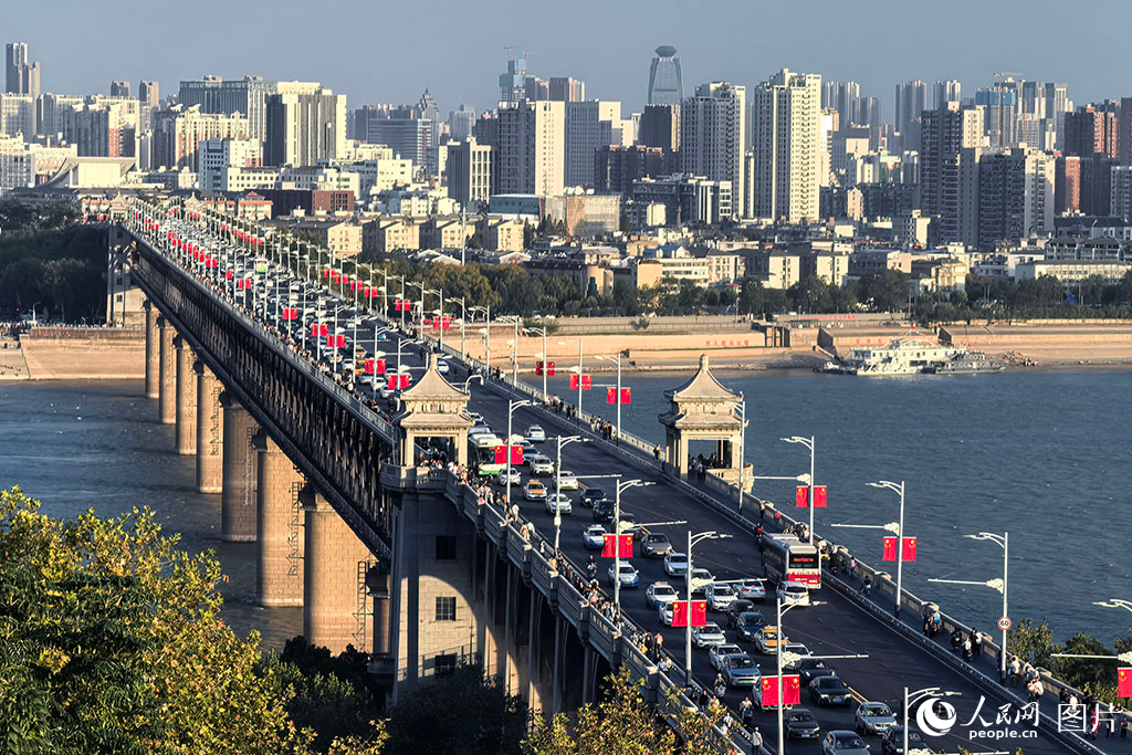 武漢長江大橋，素有“萬里長江第一橋”的美譽，是新中國橋梁建設史上的首座里程碑，開啟了中國現代化橋梁建設的輝煌篇章。大橋的建成，徹底打破了長江天塹對南北交通的阻隔，有力推動了全國南北經濟的協同發展和文化交流。它如巨龍般橫跨長江，極大便利了長江兩岸的物資流通，顯著提升了南北交通的暢通效率。國慶期間，武漢長江大橋上鮮艷的五星紅旗迎風招展，整座城市洋溢著喜慶祥和的節日氣氛，連綿的“中國紅”構成一道絢麗的風景線。人民網記者 周雯攝
