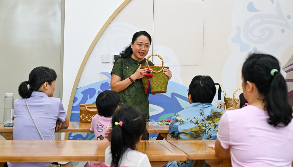 10月12日，在海南省文化館，東山草編技藝傳承人袁潔（后）為家長和小朋友講解東山草編技藝。