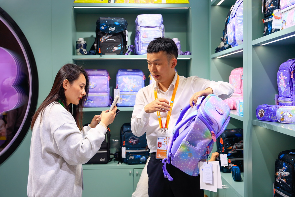 11月8日，在第八屆進博會消費品展區，觀眾（左）在一家兒童書包品牌展臺咨詢產品。新華社記者 劉佳琪 攝